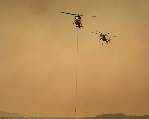 Two helicopters cycling buckets through smoke above a dip site