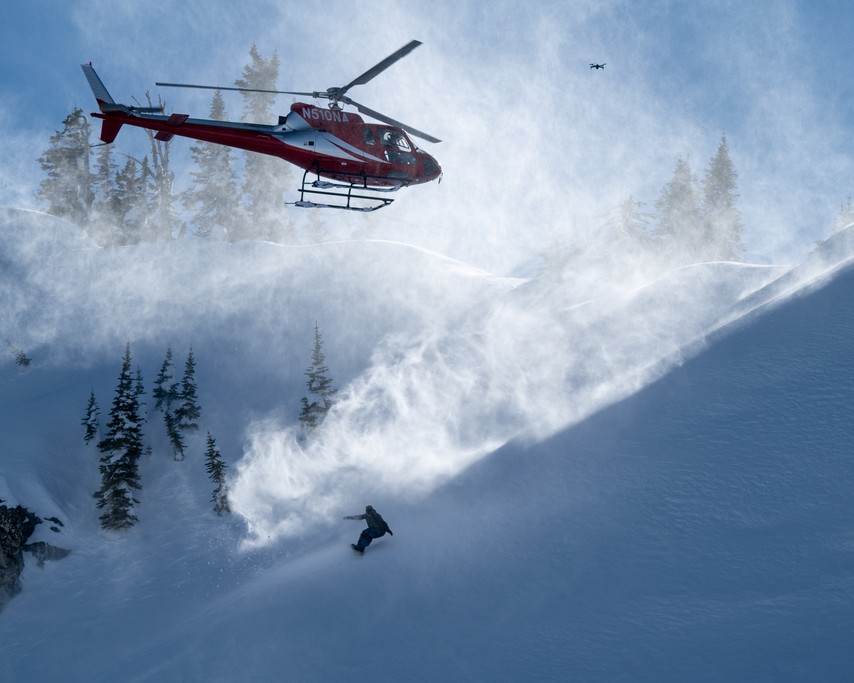 Snowboarder dropping in below the helicopter in fresh powder